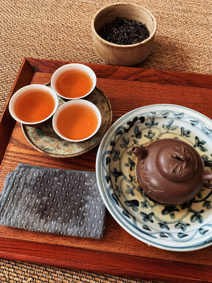 Tea set with teapot, cups, and tea leaves on a wooden tray.